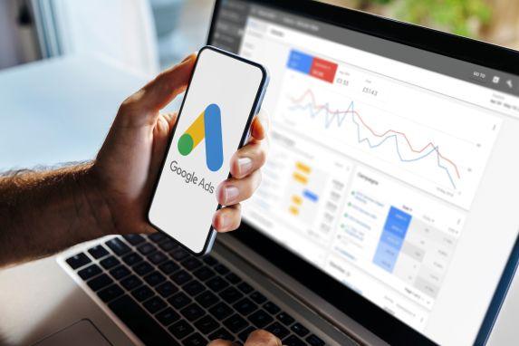 Smartphone mit Google-Ads-Logo vor Kampagnen-Dashboard – ideal für B2B/Services, Online-Shops & Marken, SaaS/Tech sowie lokale Standorte.